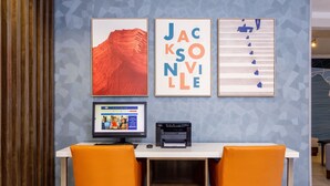 A workspace with two orange chairs, a computer, and a printer on a white table against a blue wall with geometric patterns.