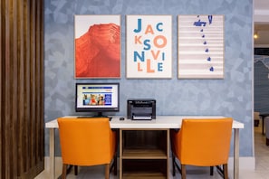 A workspace with two orange chairs, a computer, and a printer on a white table against a blue wall with geometric patterns.