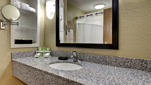 A hotel bathroom with a granite countertop sink, a large mirror, and a towel rack with towels.