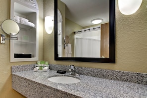 A hotel bathroom with a granite countertop sink, a large mirror, and a towel rack with towels.