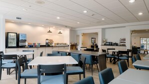 A spacious dining area with multiple tables and chairs, a kitchen area with a refrigerator and food display, and a seating area with sofas and a coffee machine. - Hotel Bethany Beach (Bethany Beach)
