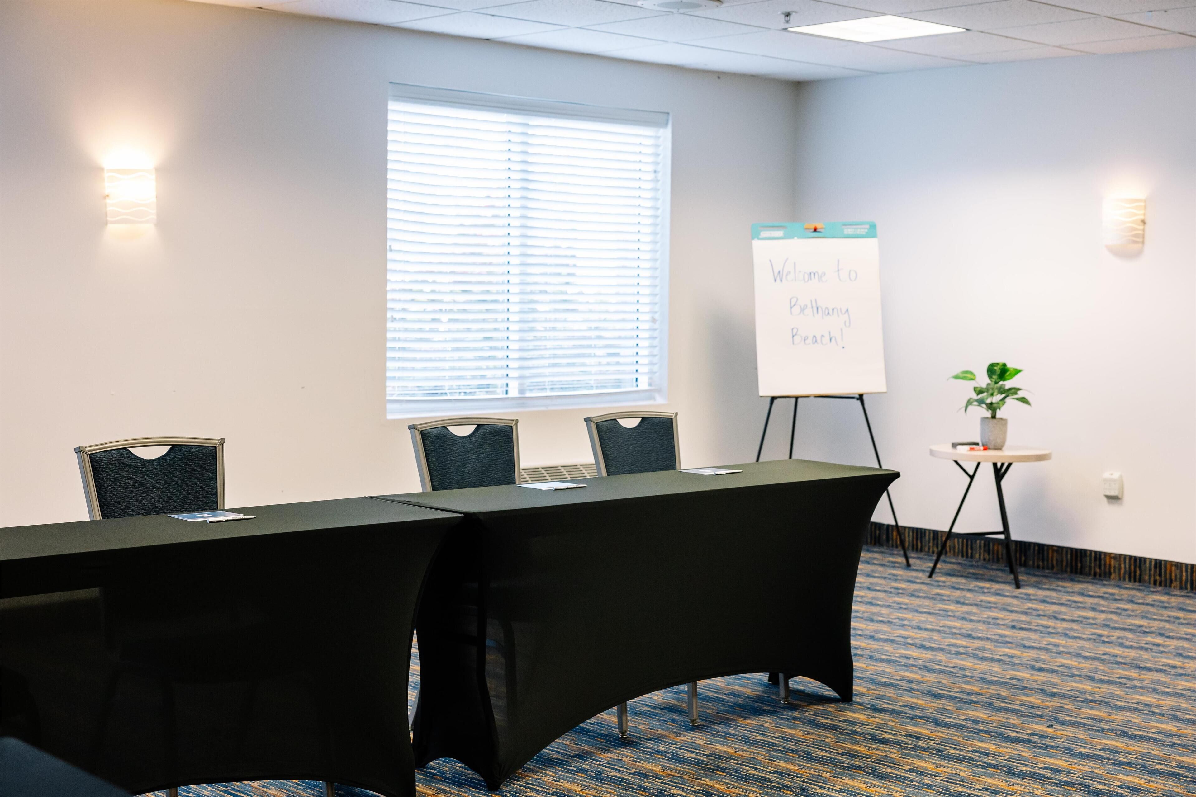 A conference room with a long table, four chairs, a whiteboard, and a potted plant.