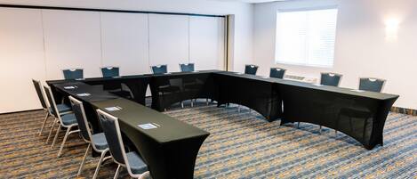 A conference room with a long table, chairs, a projector screen, and a large window.