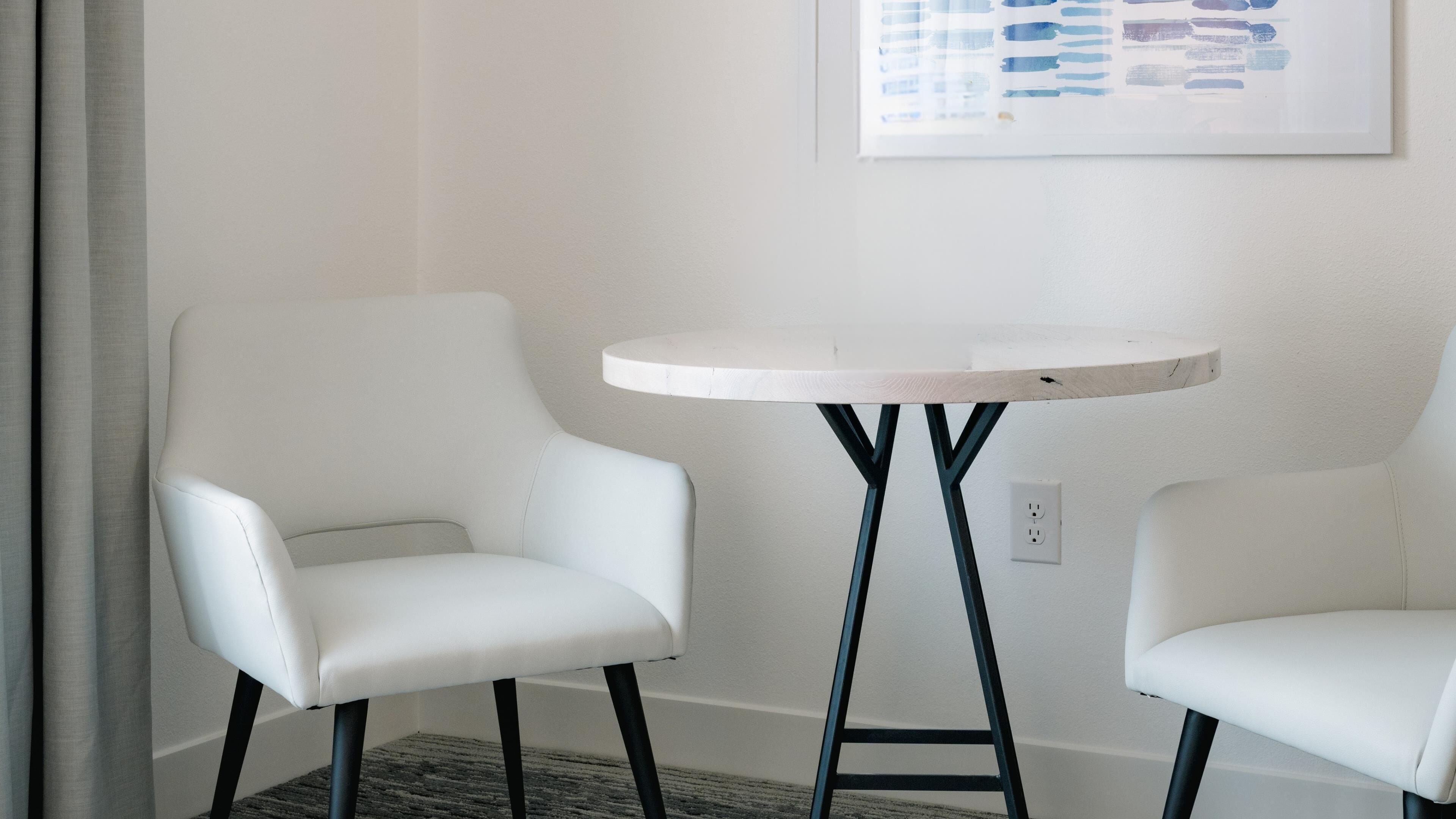 A room with two white chairs and a small round table with a white top and black legs.