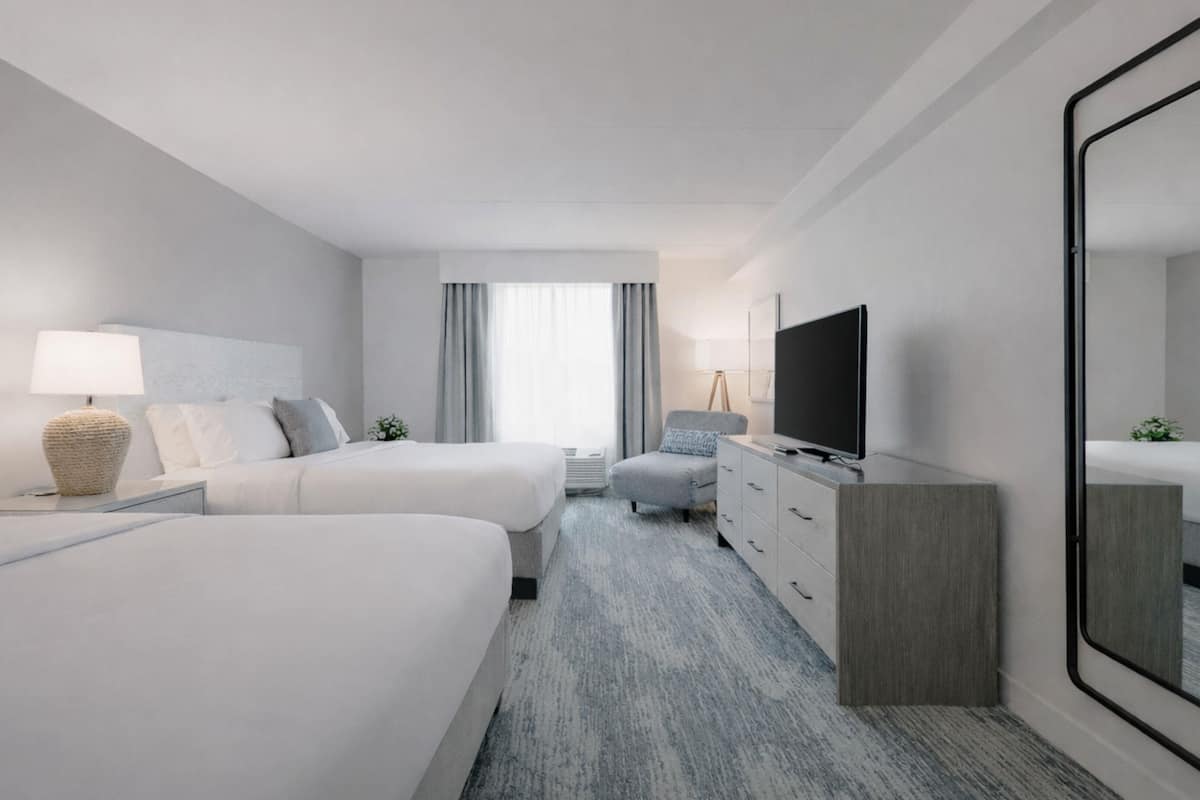 A hotel room with two beds, a TV, a dresser, and a large mirror.