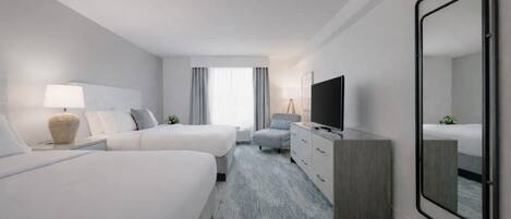 A hotel room with two beds, a TV, a dresser, and a large mirror.