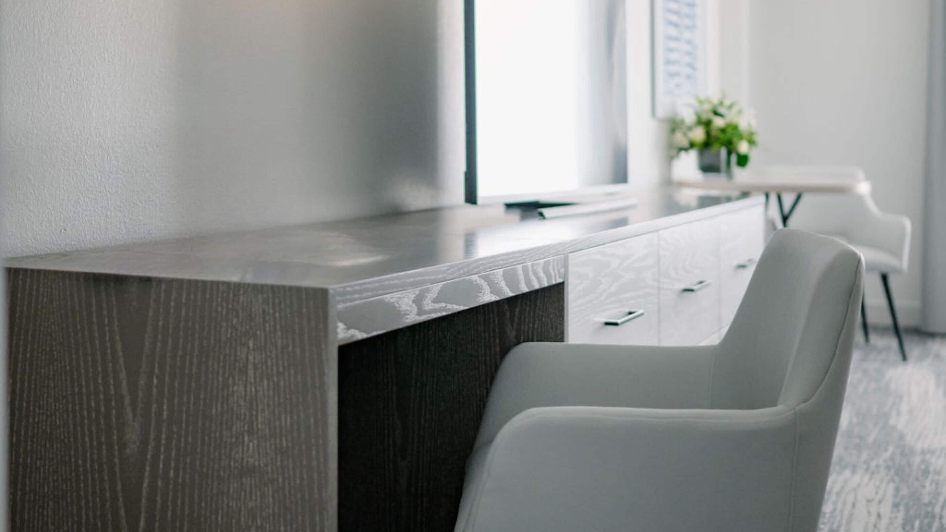 A modern office desk with a dark wood finish and a white chair.