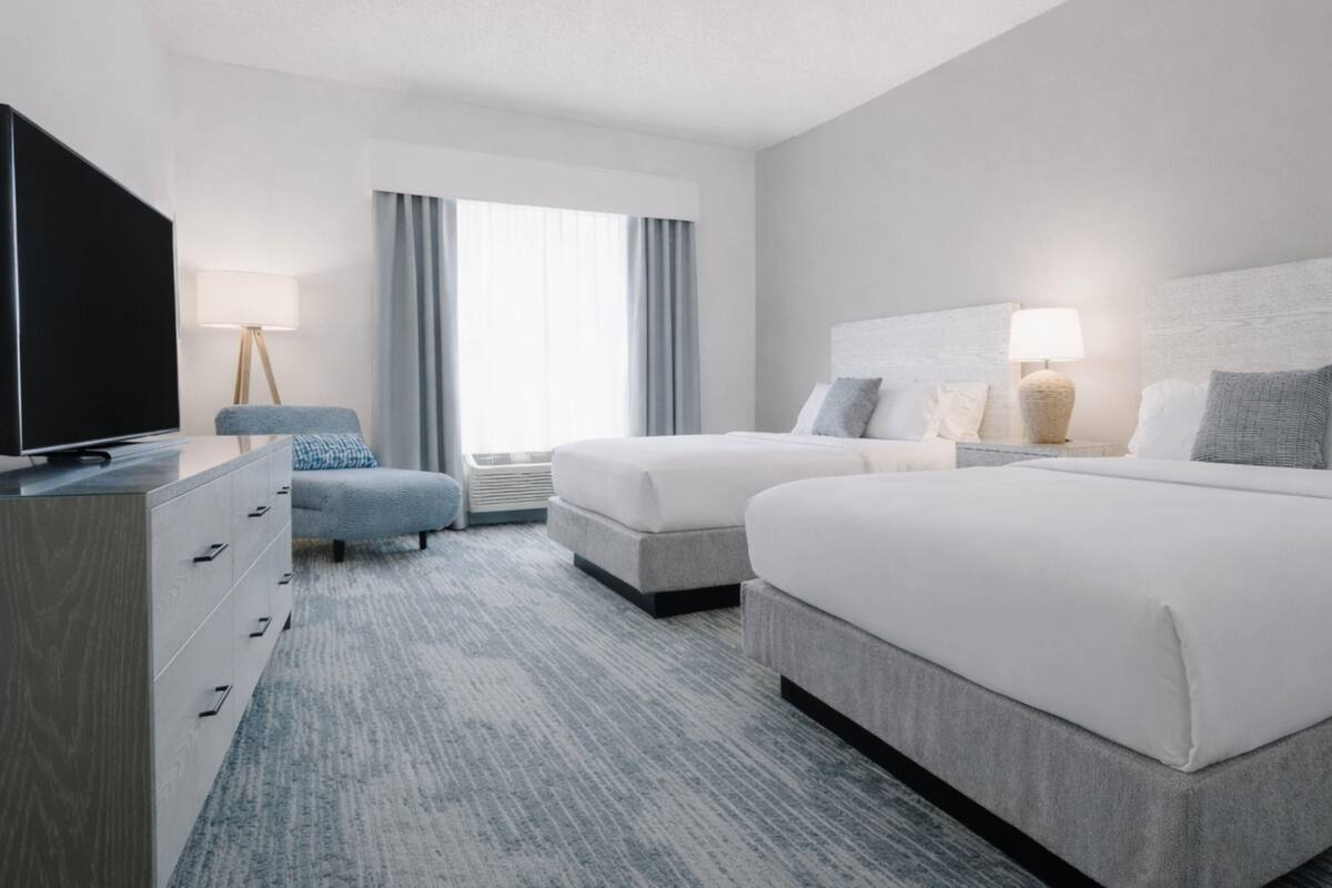 A hotel room with two beds, a TV, a desk, and a lamp.
