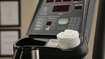 A treadmill with a control panel displaying heart rate and other metrics, a towel, and a water bottle.