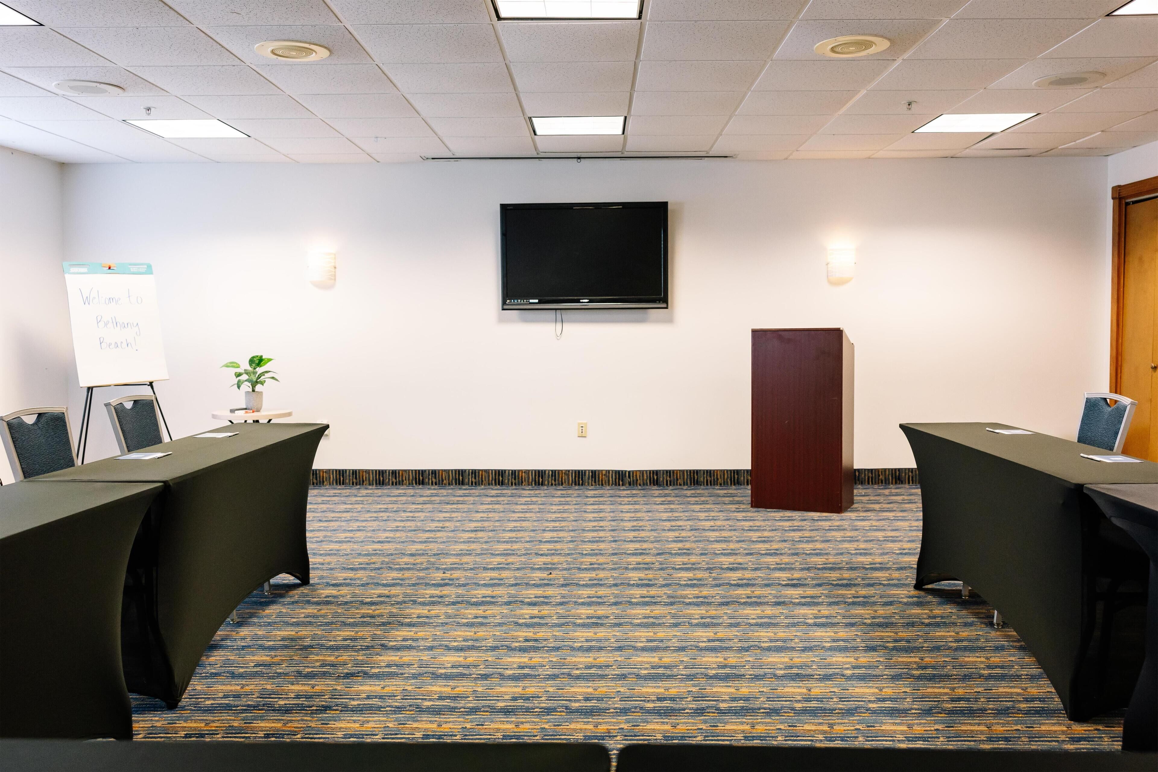 A conference room with a long table, two chairs, a whiteboard, and a TV on the wall.