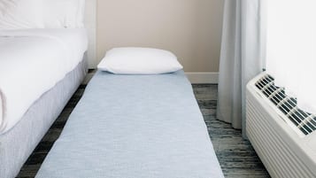 A hotel room with a bed, a bench, a window with curtains, and a wall-mounted air conditioner.