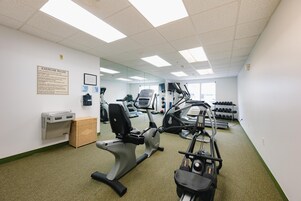 A gym with exercise machines, a mirrored wall, and a bulletin board with rules.