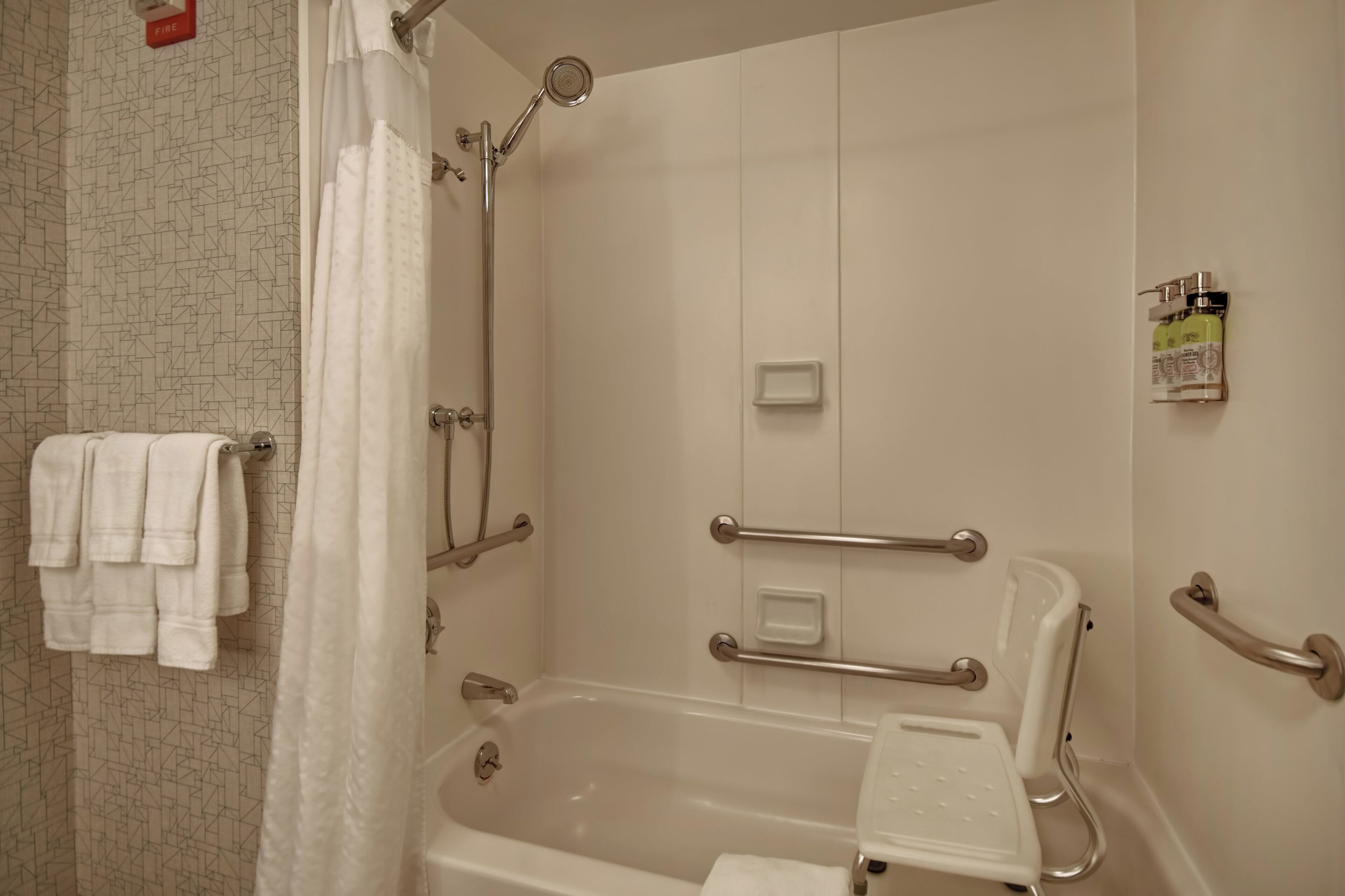 A bathroom with a bathtub, shower, and handrails.