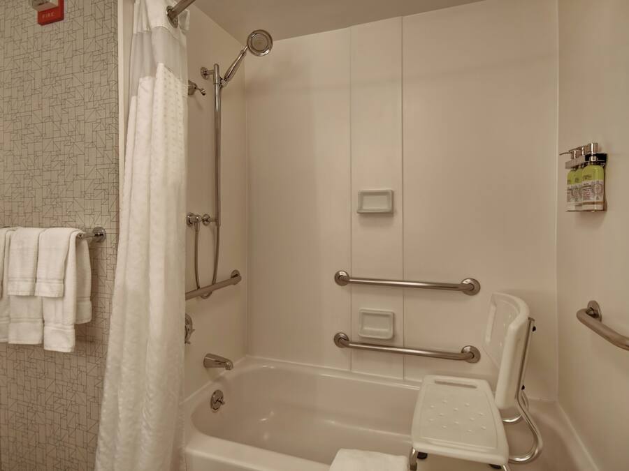A bathroom with a bathtub, shower, and handrails.