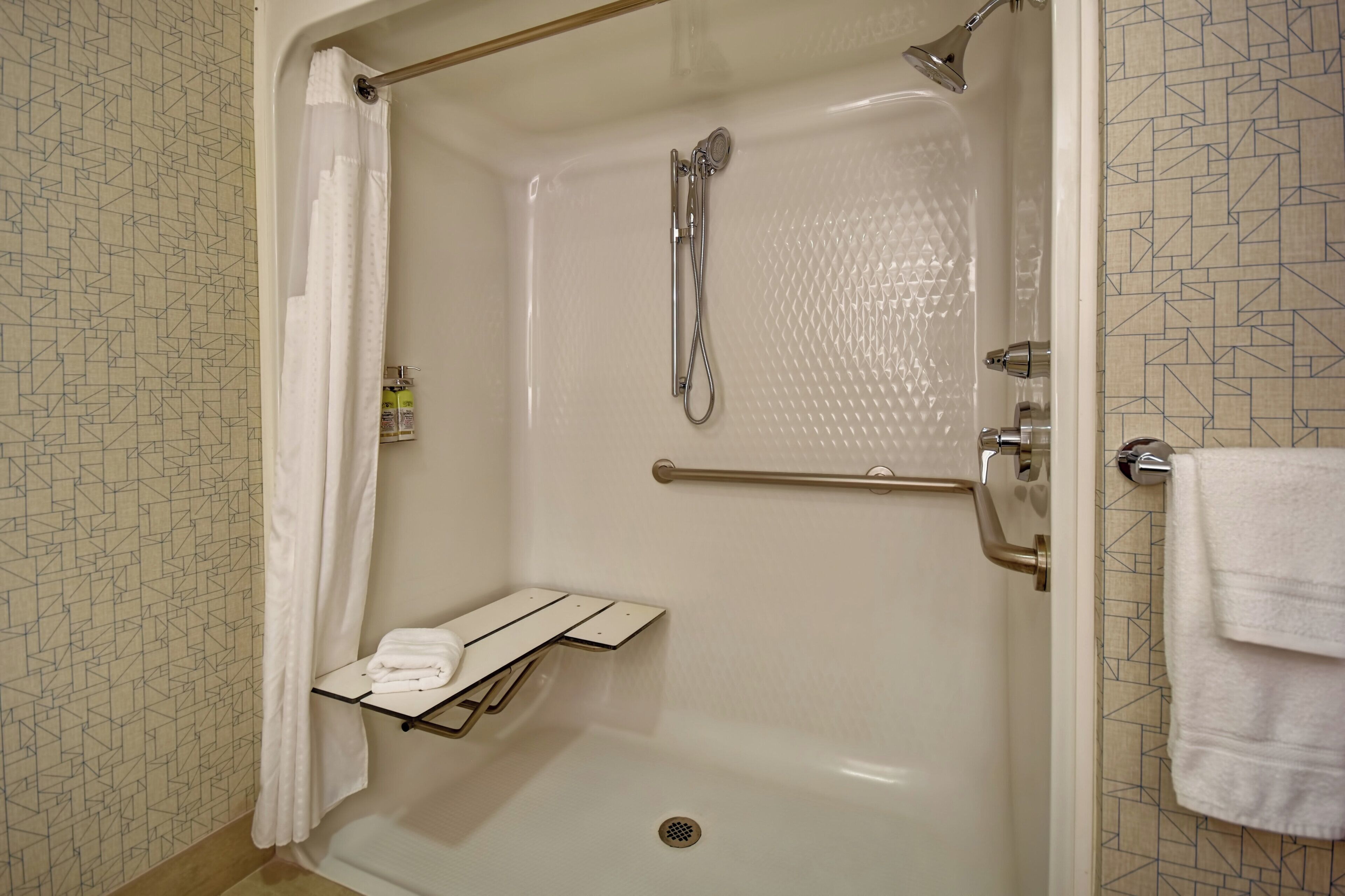 A shower with a handheld showerhead, a towel rack, and a small shelf with towels.