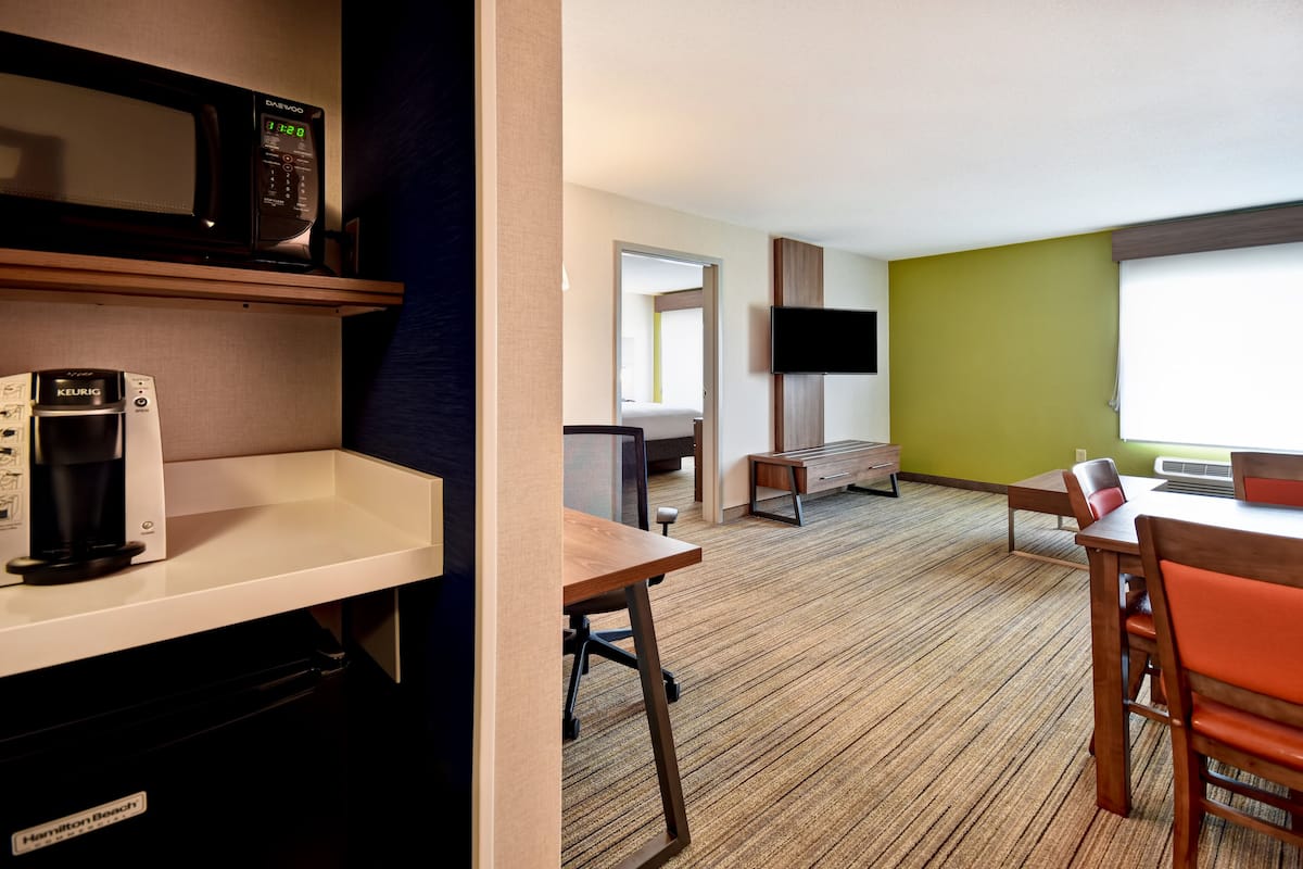 Ein Hotelzimmer mit Küchenzeile, einem an der Wand befestigten Fernseher, einem Holzespeisetisch mit Stühlen und einem großen Fenster.
