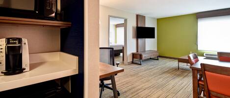 Habitación de hotel con kitchenette, televisor montado en la pared, mesa de comedor de madera con sillas y un ventanal grande.