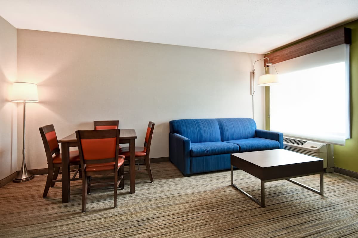 Ein Hotelzimmer mit Esstisch, Stühlen, einer Couch, einem Couchtisch und einer Lampe.
