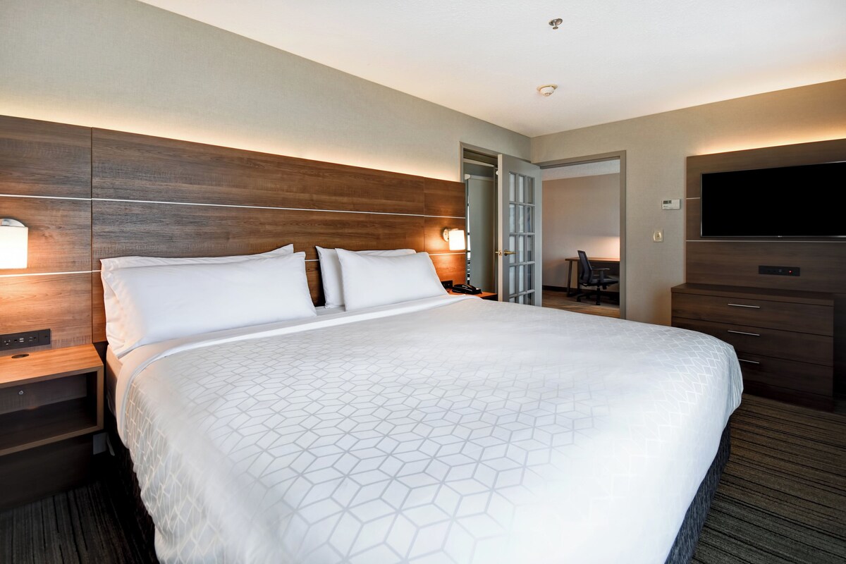 A hotel room with a large bed, wooden headboard, bedside tables, a TV, and a wardrobe.