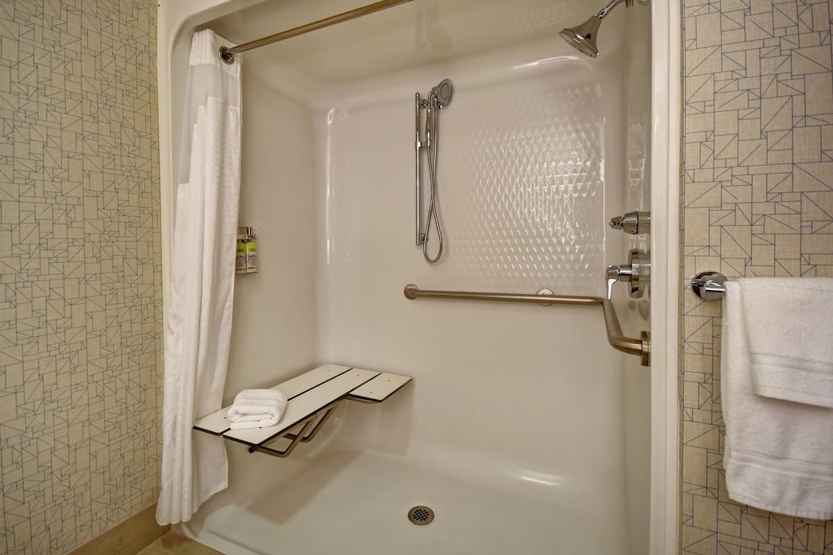Eine barrierefreie Dusche mit Glastür, Handtuchhalter und einer kleinen Ablagefläche.