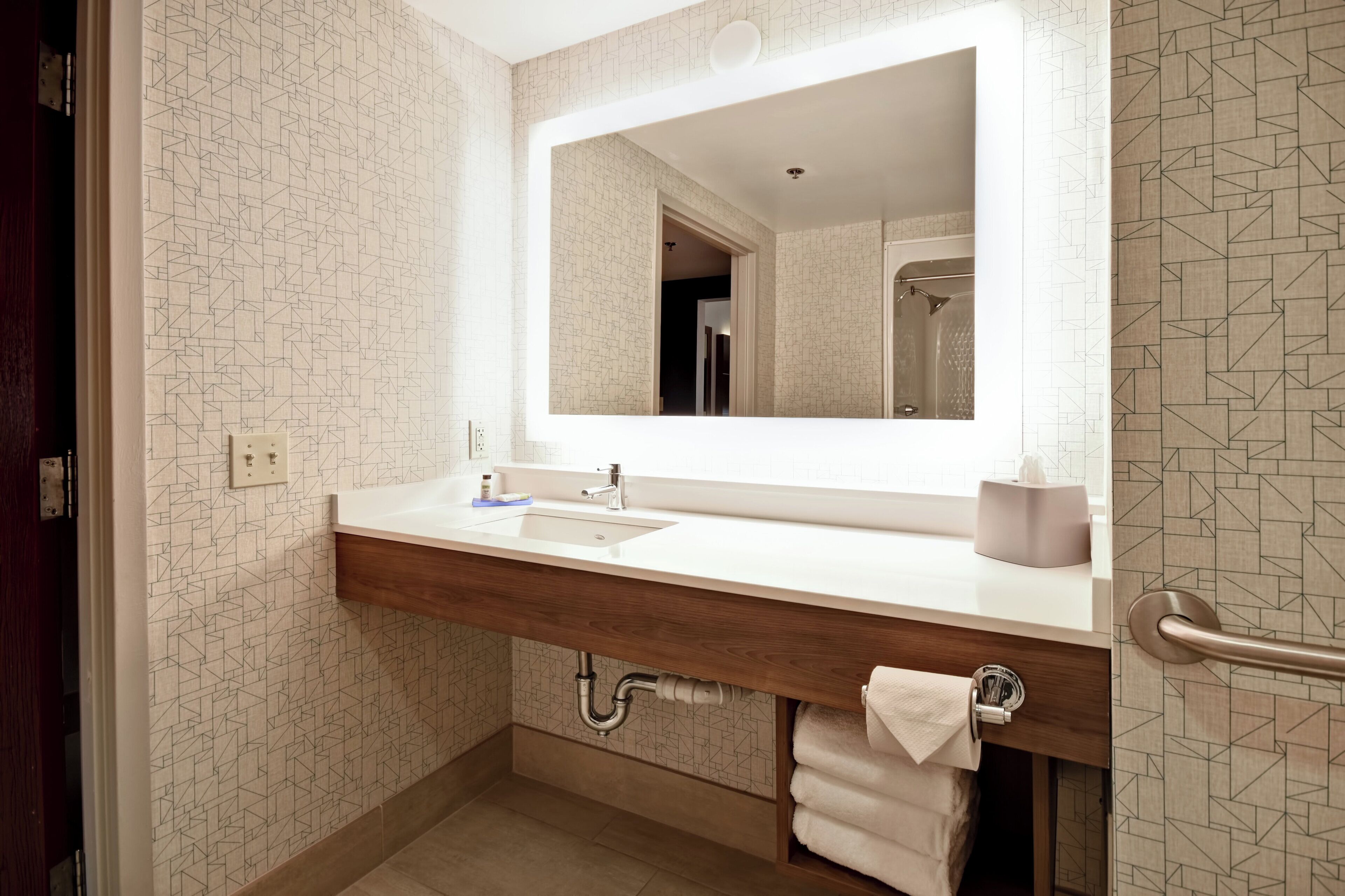 A bathroom with a large mirror, a sink, a towel rack, and a shower area.