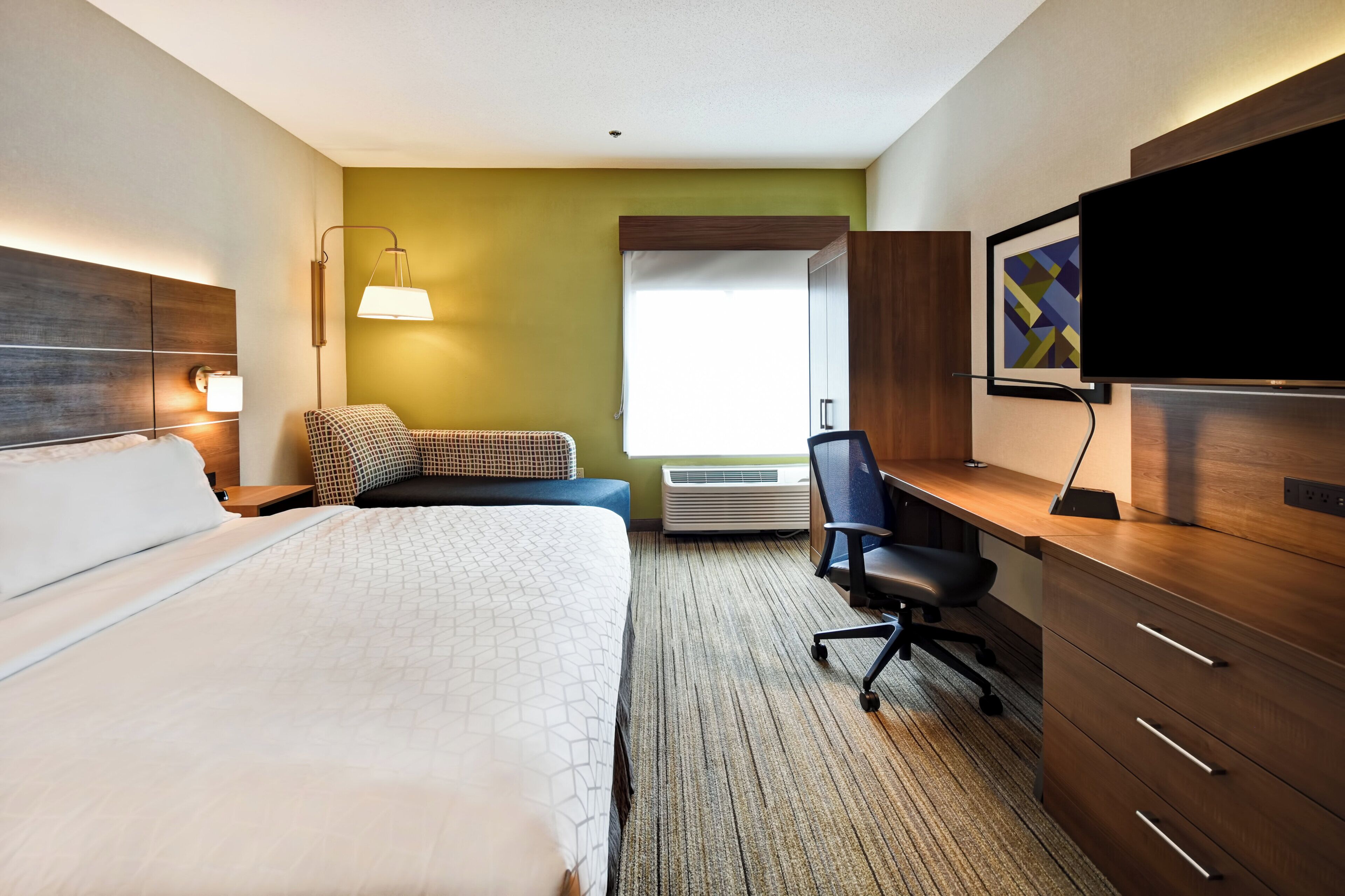 A hotel room with a bed, desk, chair, television, and a window with a view.