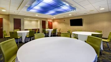 A conference room with round tables and green chairs, a flat-screen TV on the wall, and a blue ceiling design.