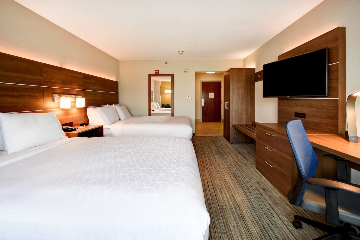 Ein Hotelzimmer mit zwei Betten, einem Schreibtisch, einem Stuhl, einem Fernseher und einem durchgegangenen Tür sichtbaren Badezimmer.