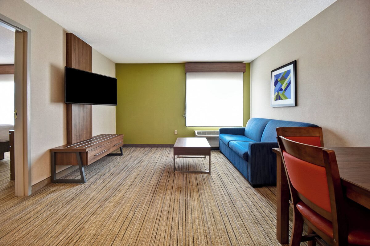 A modern living room with a flat-screen TV, a blue sofa, a wooden coffee table, and a dining area with a wooden table and chairs.