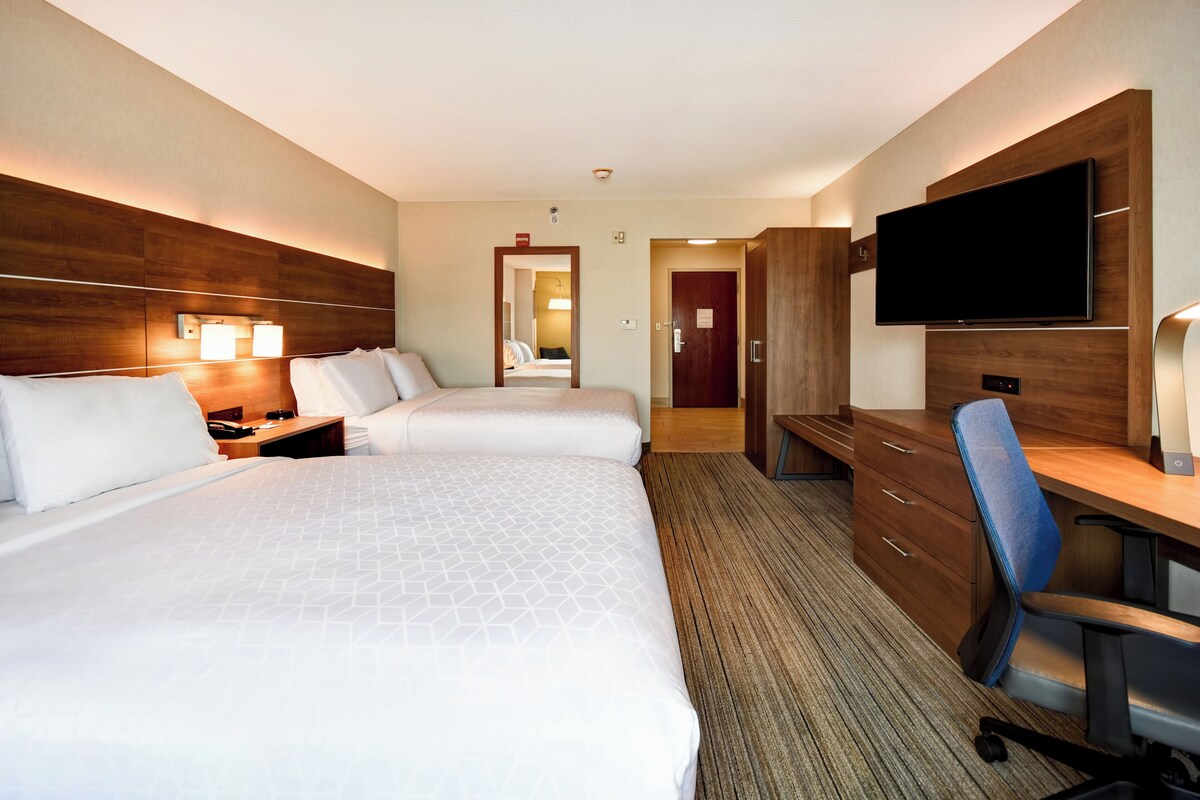 A hotel room with two beds, a desk, a chair, a TV, and a bathroom visible through an open door.