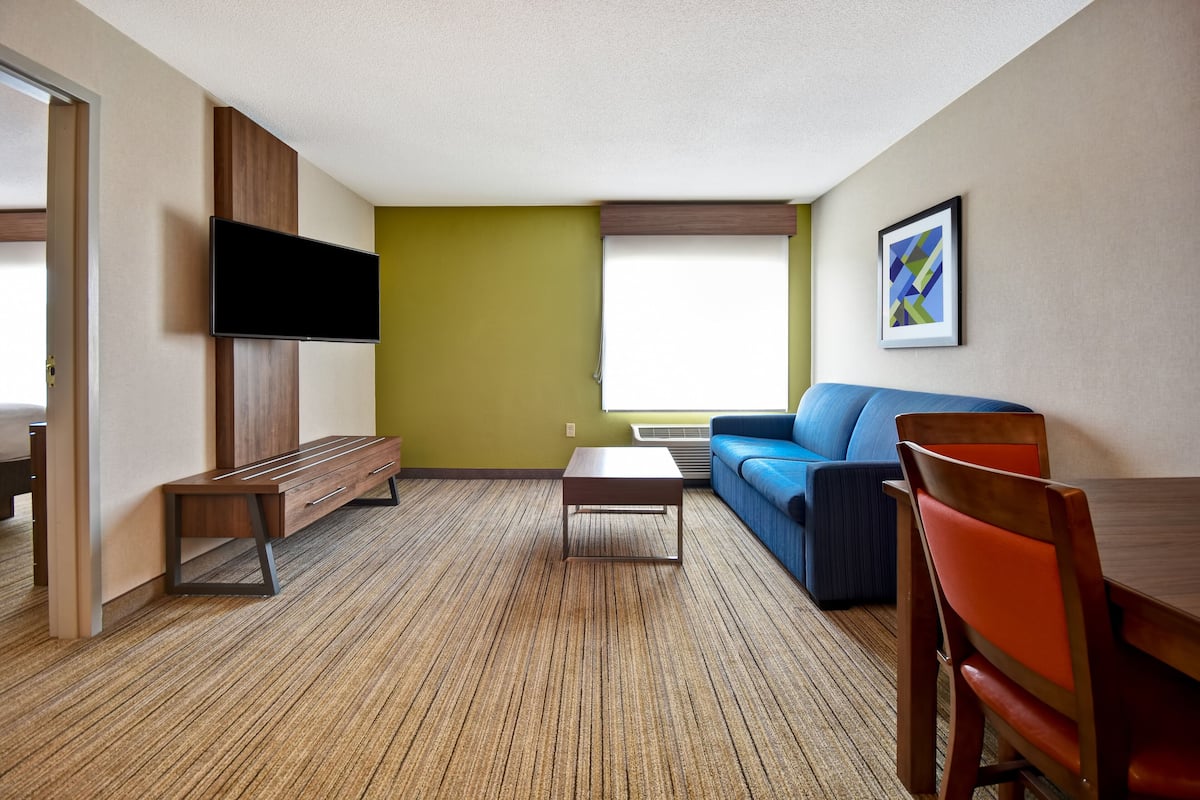 Ein modernes Wohnzimmer mit Flachbildfernseher, einem blauen Sofa, einem Holztisch und einem Essbereich mit Holztisch und Stühlen.