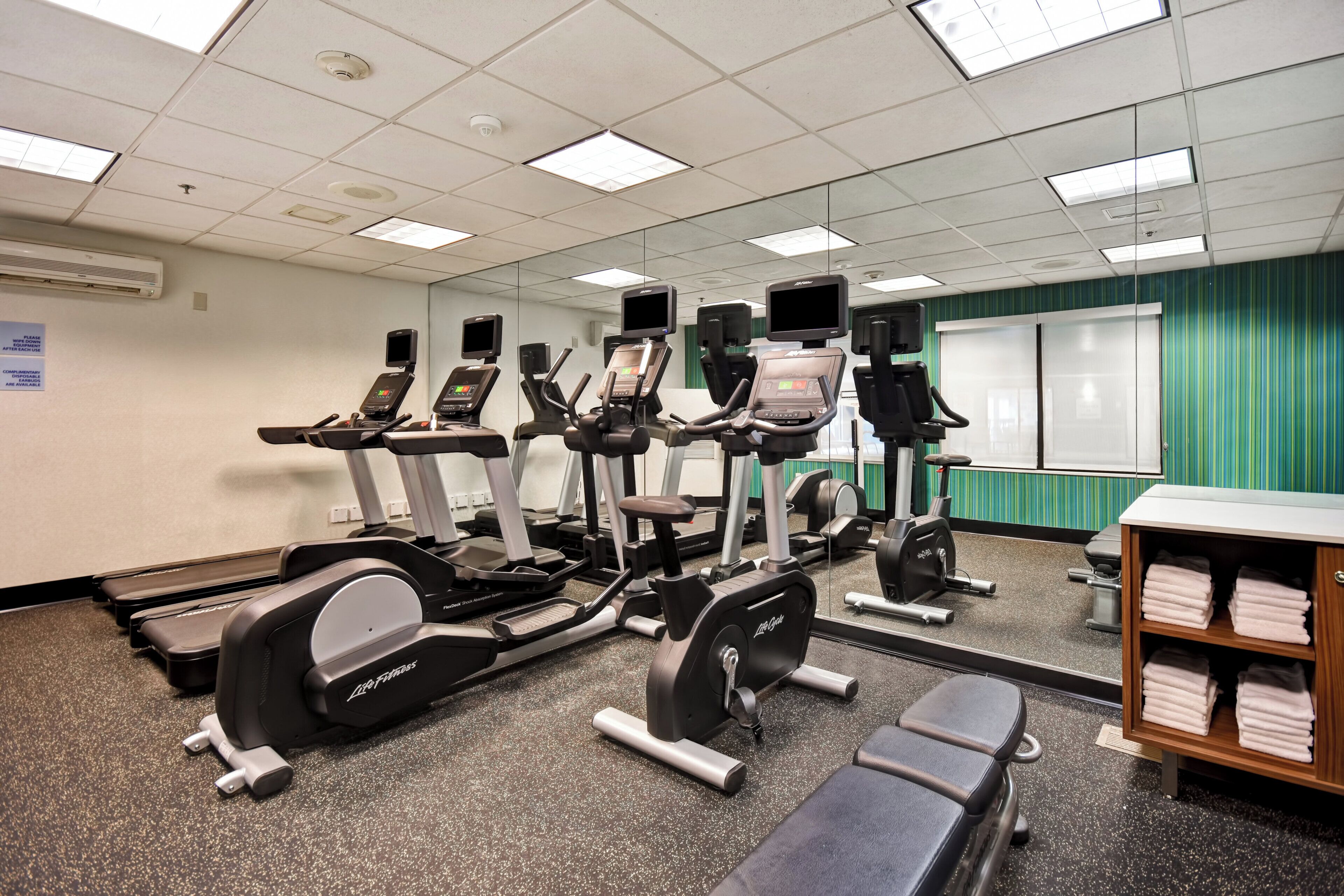A fitness center with treadmills, elliptical machines, and a bench area.