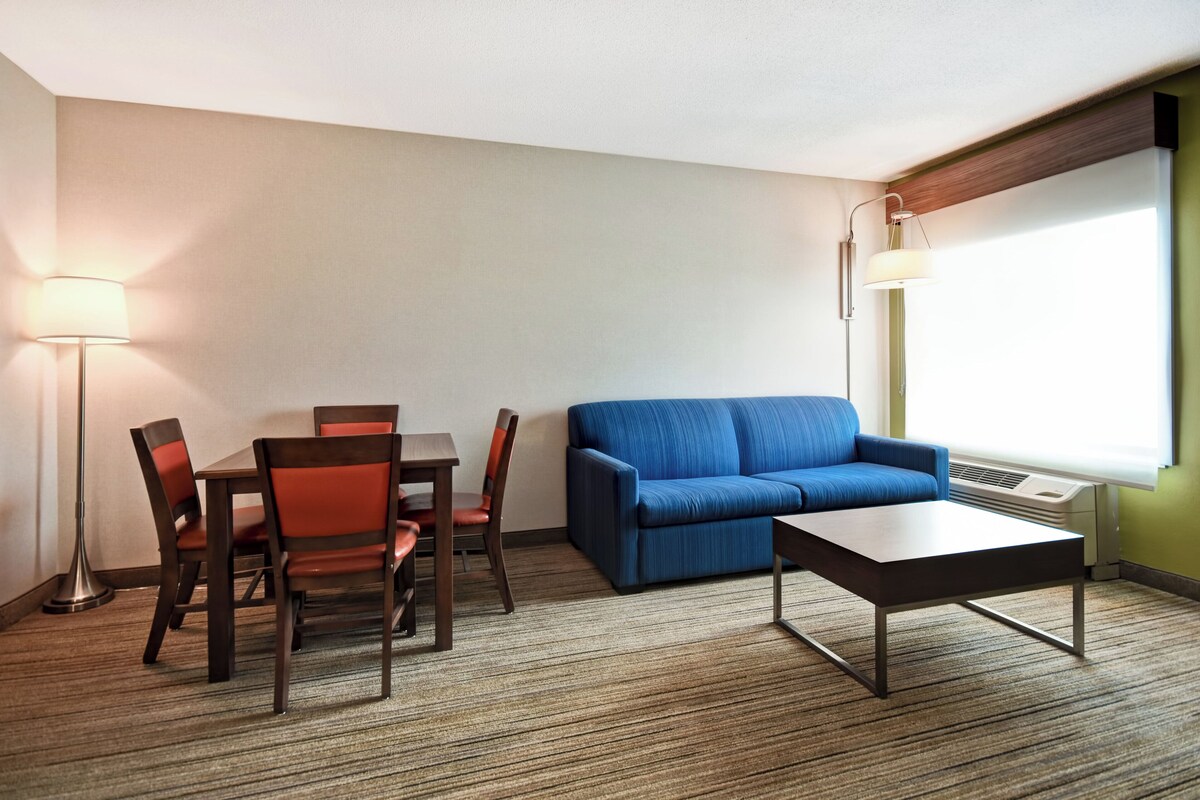 A hotel room with a dining table, chairs, a sofa, a coffee table, and a lamp.