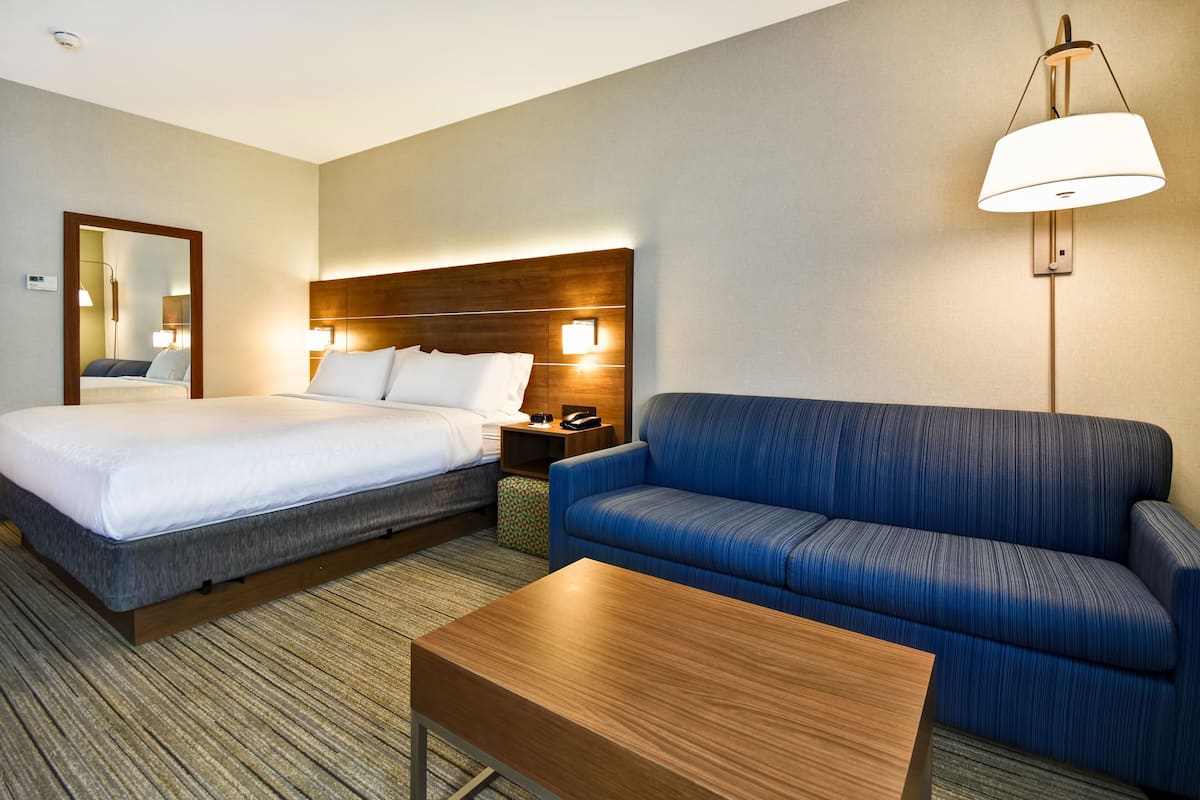 Ein Hotelzimmer mit Bett, einer Sitzecke, einem Nachttisch, einer Lampe und einem Spiegel.