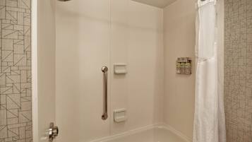 Un baño con ducha a nivel, barras de apoyo y una bañera blanca.
