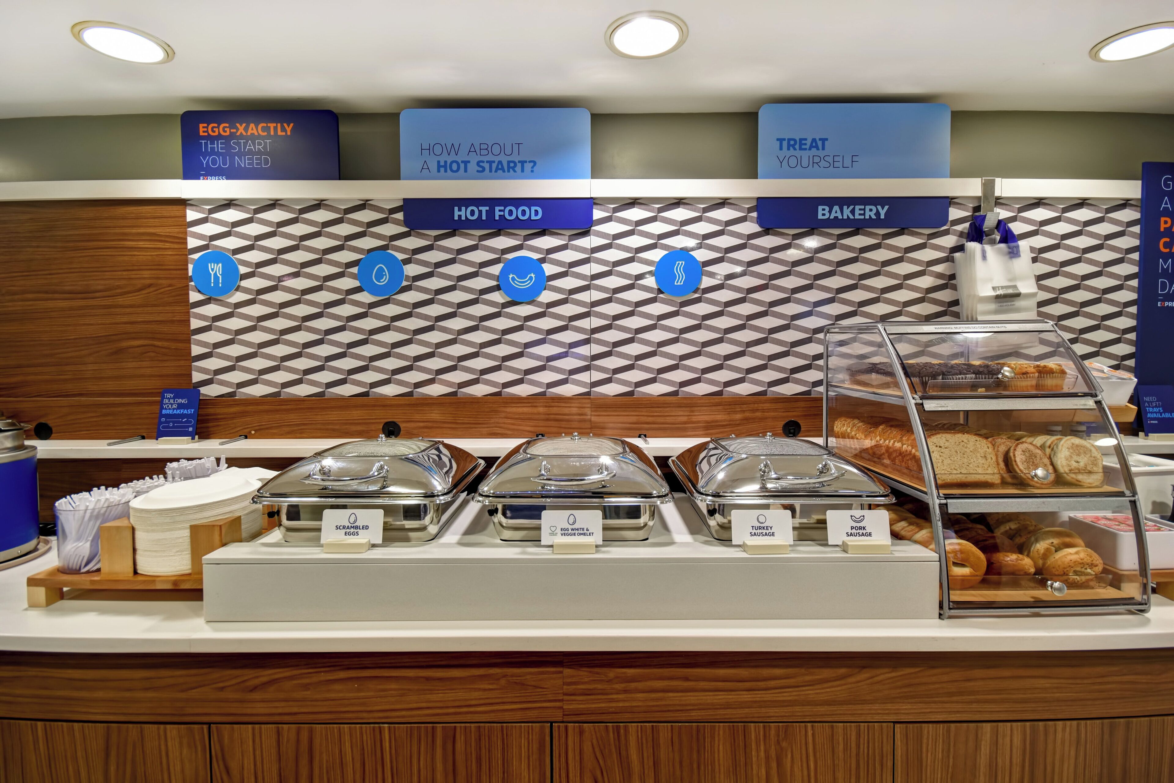 A breakfast buffet area with labeled sections for scrambled eggs, egg white and veggie omelet, turkey sausage, and pork sausage.