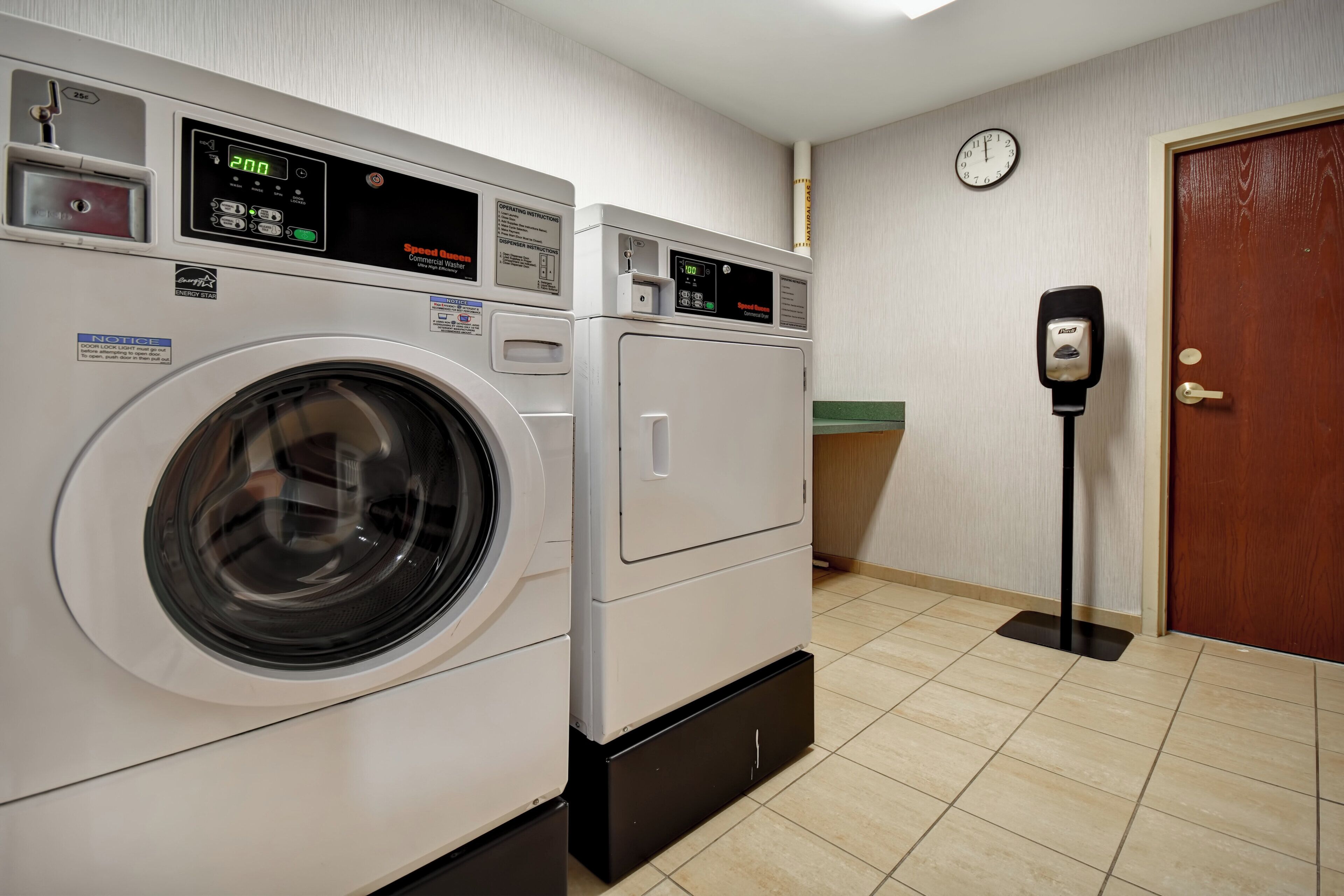A laundry room with two stacked washers and dryers, a clock on the wall, and a door with a lock.