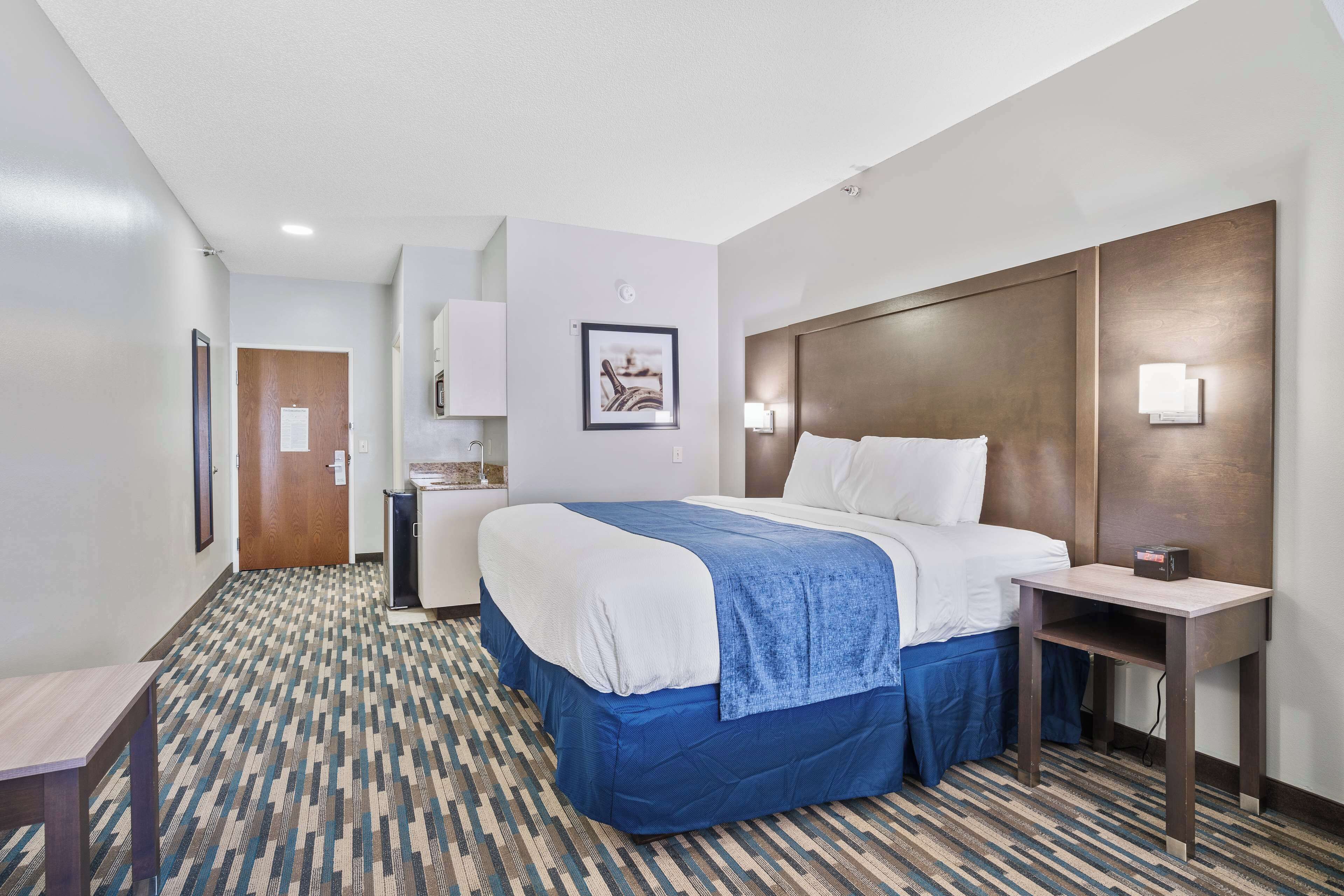 A hotel room with a large bed, a desk, a chair, and a small table.