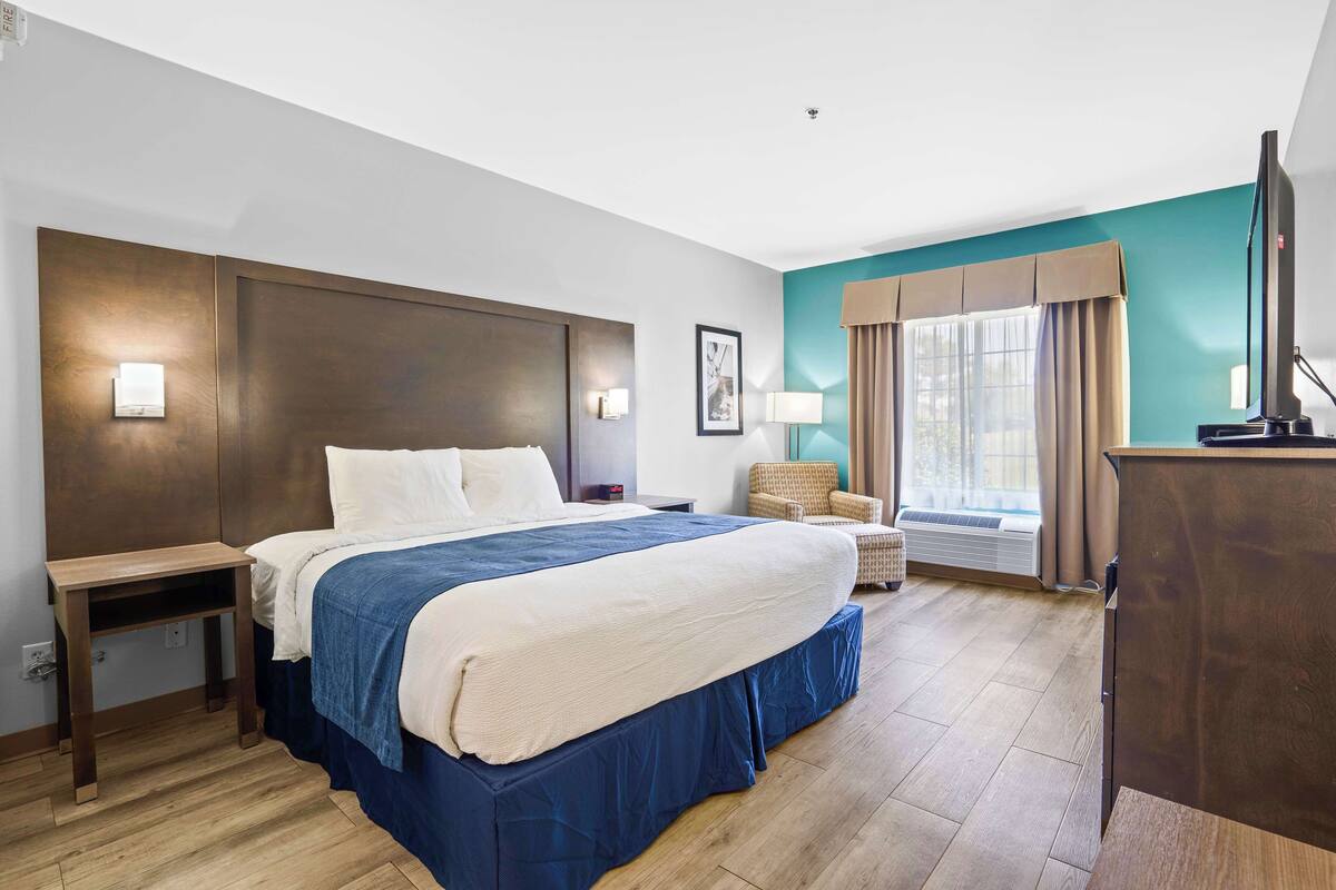 Een hotelkamer met een groot bed, een bureau, een stoel, een televisie en een raam met gordijnen.