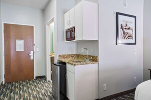 Habitación de hotel con kitchenette, microondas, lavamanos y una puerta con un aviso.