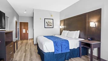 A hotel room with a bed, bedside table, TV, and a picture on the wall.
