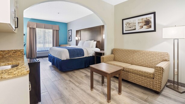 A hotel room with a bed, a sofa, a small table, a sink, and a window with curtains. - Blue Water Inn & Suites, BW Signature Collection (Sneads Ferry)