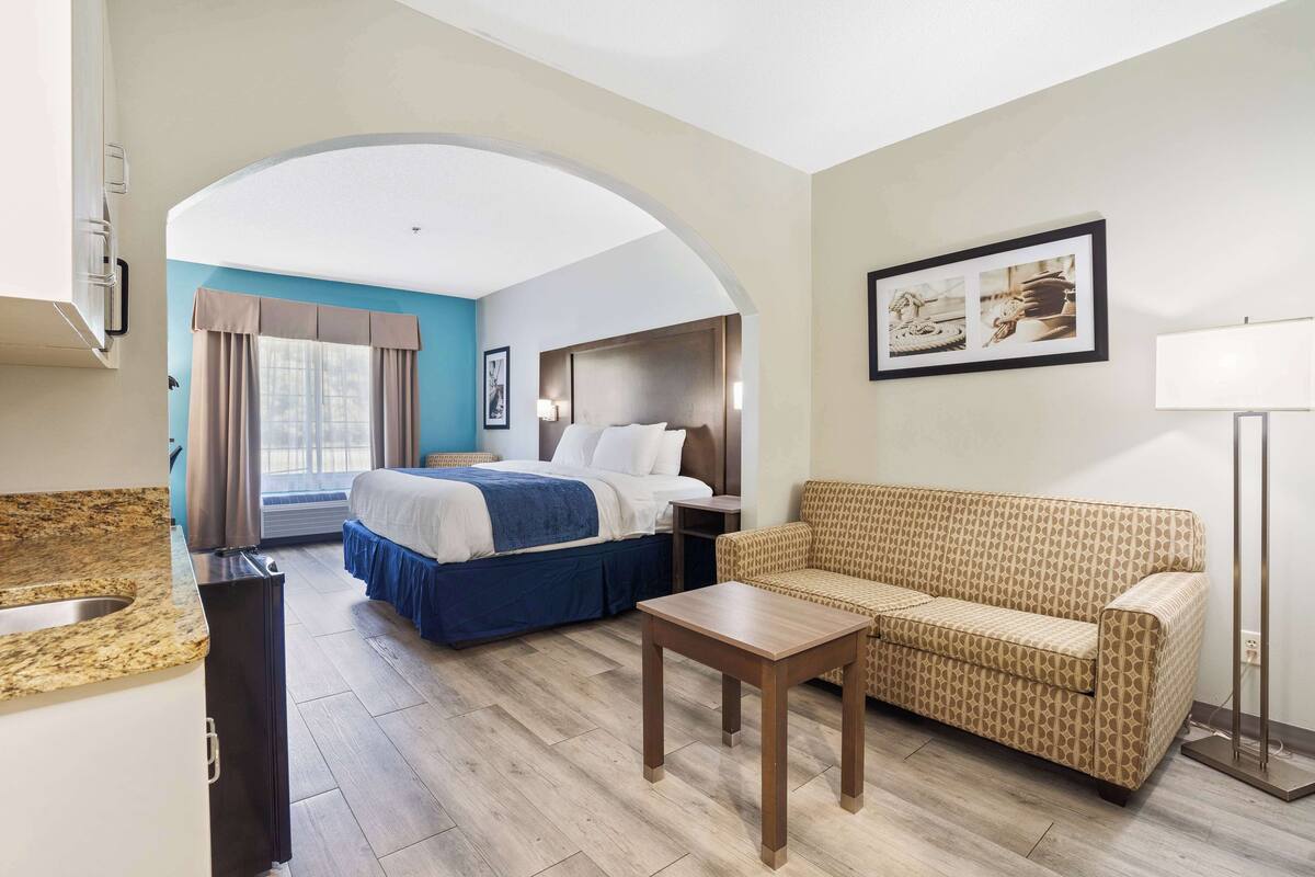 Een hotelkamer met een bed, een slaapbank, een klein tafeltje, een wastafel en een raam met gordijnen.