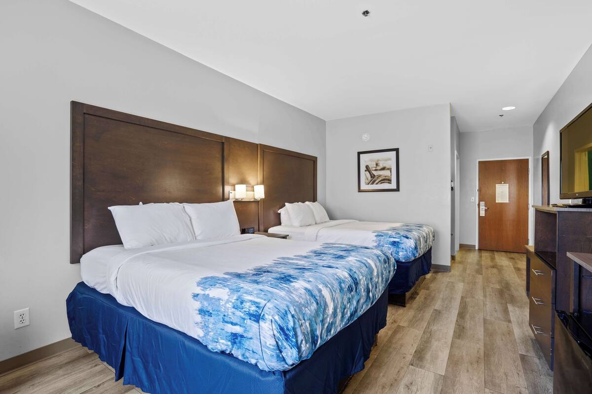 Een hotelkamer met twee bedden, een houten hoofdeinde, een ingelijst schilderij aan de muur en een houten vloer.