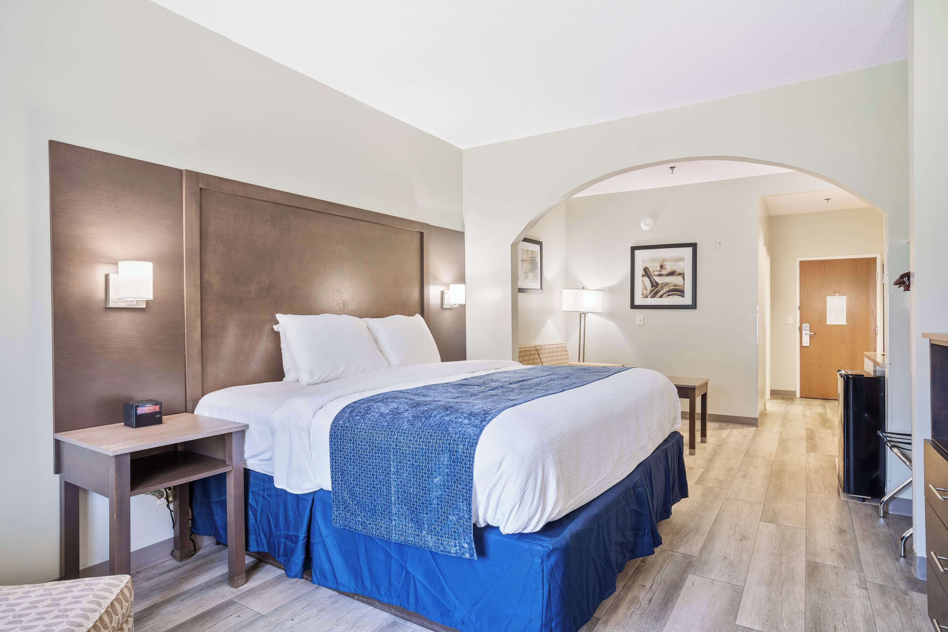 A hotel room with a large bed, a bedside table, a desk, a lamp, and a TV.