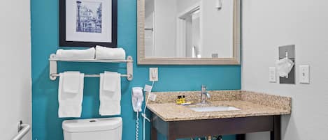 A bathroom with a white toilet, a sink with a granite countertop, a mirror, and a towel rack with two white towels.