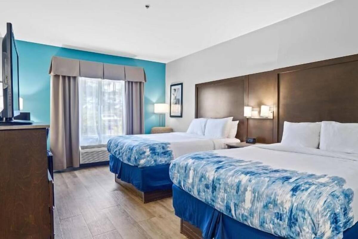 Een hotelkamer met twee bedden, een bureau, een televisie en een raam met gordijnen.