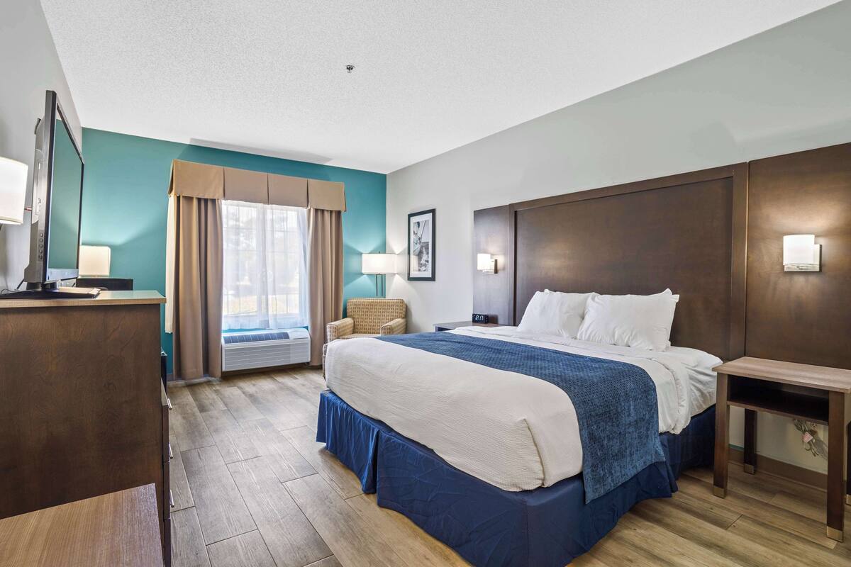 Een hotelkamer met een groot bed, een bureau, een flatscreen televisie, een stoel en een raam met gordijnen.