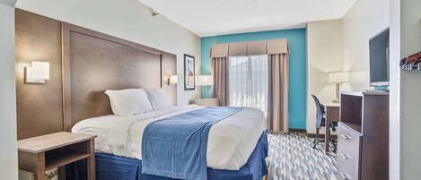 A hotel room with a bed, bedside table, desk, chair, and a TV.