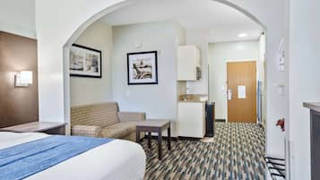 A hotel room with a bed, a sofa, a small table, a kitchenette, and an arched doorway leading to another room.